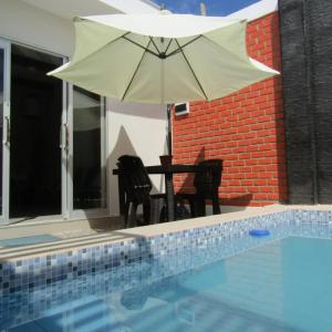 einen Tisch und Stühle unter einem Sonnenschirm neben einem Pool in der Unterkunft MERINO HOUSE COLAN BEACH in Paita