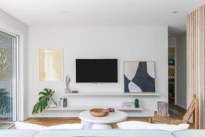 a living room with a white couch and a tv at The Pool House - Byron Bay in Byron Bay