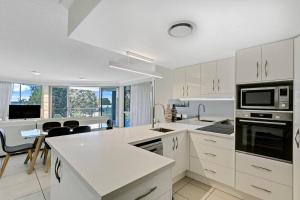 une cuisine avec des armoires et des appareils blancs et une table dans l'établissement Modern Cotton Tree Apartment With Views, à Maroochydore