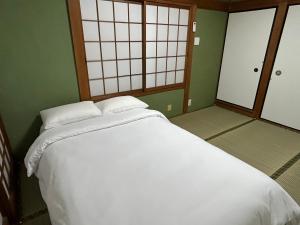 泉佐野市にあるKIX House Waraku III 和楽三号館の緑の壁の客室で、白い大型ベッド1台が備わります。