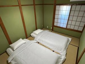 a small room with two beds and two windows at KIX House Waraku III 和楽三号館 in Izumi-Sano