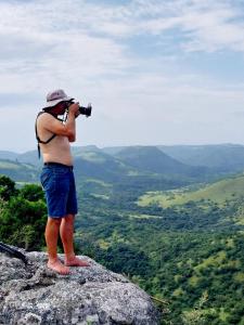 un hombre sosteniendo una cámara en la cima de una montaña en Louis at Magwa Falls, en Lusikisiki