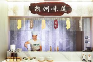 Atour X Hotel Hangzhou Binjiang Jiangnan Avenue في هانغتشو: شيف واقف في مطبخ يحضر طعام