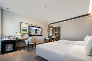 天津市にあるAtour Hotel Tianjin Zhongbei Haitai Industrial Parkの白いベッドとデスクが備わるホテルルームです。