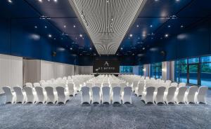 una sala de conferencias con sillas blancas y un escenario en A T HOUSE Shanghai Xujiahui en Shanghái