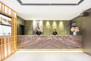 two people standing behind a marble counter in a lobby at Atour X Hotel Shanghai Central Bailian Tongchuan Road Station in Shanghai