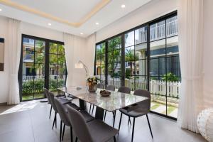 a dining room with a table and chairs and large windows at Villa Wonderland Hồ Tràm LUXURY in Ho Tram