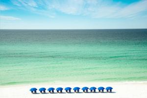 eine Gruppe von Personen mit blauen Sonnenschirmen am Strand in der Unterkunft Beal House Fort Walton Beach, Tapestry Collection By Hilton in Fort Walton Beach