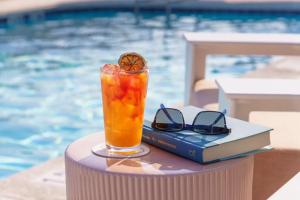 ein Buch und ein Getränk auf einem Tisch in der Nähe eines Pools in der Unterkunft Beal House Fort Walton Beach, Tapestry Collection By Hilton in Fort Walton Beach