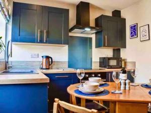 eine Küche mit blauen Schränken und einem Holztisch mit Weingläsern in der Unterkunft No. 3 A cosy spot for 4 in Cawood