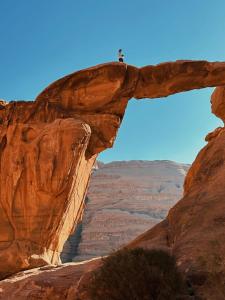 a person standing on top of a arch in the desert at Climbers House in Wadi Rum in Wadi Rum