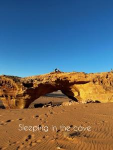 a rock arch in the desert with the words sleeping in the cave at Bedouin experiences in Aqaba