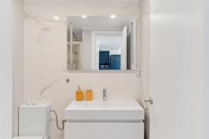 a white bathroom with a sink and a mirror at Sunny Beachfront Apt in Costa da Caparica in Almada