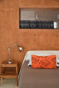 a bed with an orange pillow and a lamp on a table at Herdade Reguenguinho in Cercal