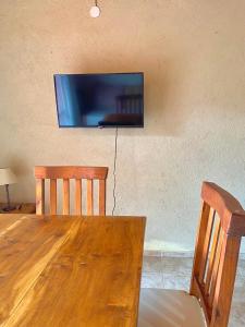 TV en la pared con mesa de madera y 2 sillas en Cabañas Villa Luz en Salsipuedes