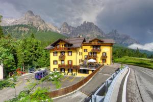 ein großes gelbes Gebäude mit Bergen im Hintergrund in der Unterkunft GH Hotel Fratazza in San Martino di Castrozza