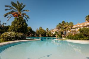 une grande piscine avec un palmier et des bâtiments dans l'établissement Cozy holiday home in Dama de noche in Puerto Banús, à Marbella