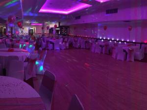 un salón de banquetes con mesas y sillas blancas e iluminación púrpura en Kings Park Hotel, en Glasgow