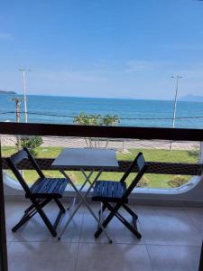 a table and two chairs on a balcony with the ocean at Ap Vista Mar em Caraguatatuba in Caraguatatuba