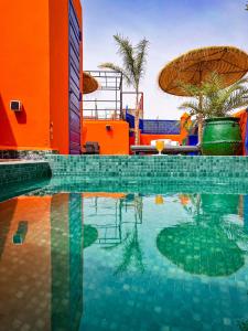 a swimming pool with an orange building and an umbrella at Riad Le Jardin de Lea, Suites & Spa in Marrakesh