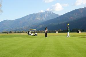 dos personas de pie en un campo de golf con un carrito de golf en Hotel Nassfeld, en Sonnenalpe Nassfeld