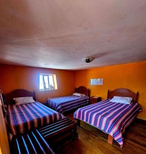 two beds in a room with orange walls at KanchayKillaWasi in Chinchero