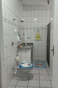 a white tiled bathroom with a toilet and a sink at CASA de 2 QUARTOS in Guaratinguetá