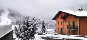 een huis met sneeuw op de grond naast twee bomen bij Appartamenti Flora Alpina in Temù