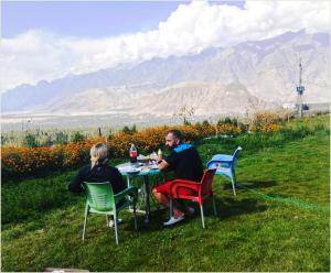 a man and woman sitting at a table in the grass at Hotel Mountain Lodge Skardu in Skardu