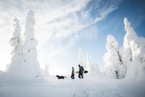 due persone e un cane che cammina in una foresta innevata di Ruka Peak - Boutique Hotel & Restaurant a Ruka