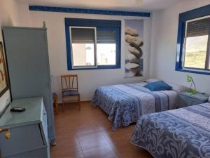 a bedroom with two beds and a chair and two windows at Casa La Fabriquilla en Cabo de Gata, Almería, Spain in Almería