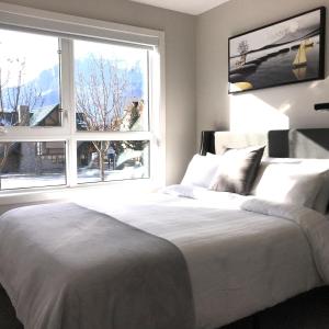 a bedroom with a white bed and a large window at Mountain Retreat: Brand New 2BR Condo in Canmore