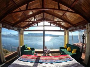 a room with a bed and chairs and a view of the water at Luna Titicaca Bungalows in Puno