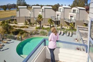a woman standing on a balcony looking at a swimming pool at Corrigans Cove in Batemans Bay