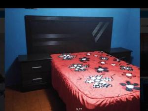a red bed with a red comforter with flowers on it at Departamento Completo en el Sur in León