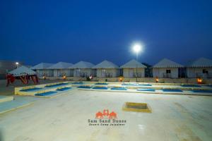 a swimming pool in front of some huts at night at Sam Sand Dunes Desert Safari Camp in Jaisalmer