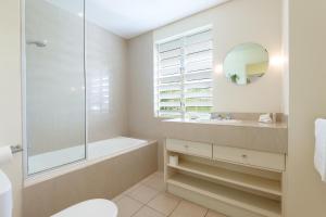 een badkamer met een bad, een wastafel en een spiegel bij Verandahs Boutique Apartments in Port Douglas