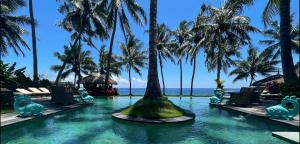 - une piscine dans un complexe avec des palmiers et l'océan dans l'établissement Louka Beach Bali, à Tianyar
