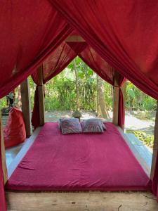 een bed in een rode tent met een roze deken bij Didu's Homestay Bed & Breakfast in Banyuwangi