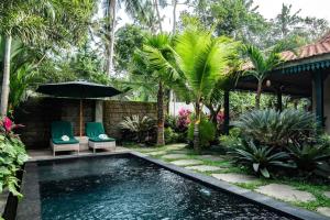 a swimming pool in a yard with two chairs and an umbrella at Cozy Jungle View 1-Bedroom Villa with Private Pool in Ubud