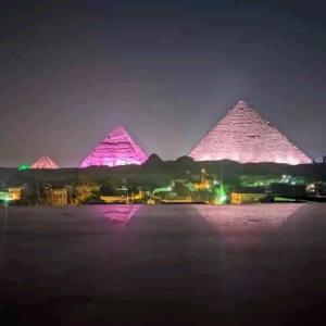 a group of pyramids are lit up at night at Store pyrmids view in Cairo