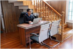 a man sitting at a desk with a laptop at White House Cottage in Kolur +3 photos