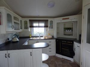 una cocina con armarios blancos y encimeras negras en Cedar Lake 58 at Southview Leisure Park, en Skegness