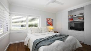 a white bedroom with a bed and a tv at The Patonga Pearl in Patonga