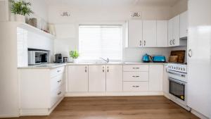 a white kitchen with white cabinets and a window at Bangalow Beach House - Ettalong, pet friendly, walk to beach,shops,cafes in Ettalong
