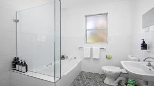 a white bathroom with a shower and a toilet and a sink at Beach Bay and Bush at Killcare in Killcare