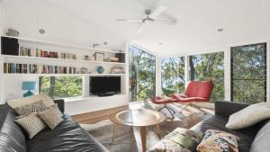 ein Wohnzimmer mit einem Sofa, Stühlen und Fenstern in der Unterkunft Treetops@Wagstaffe in Ettalong Beach