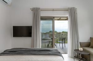 a bedroom with a bed and a tv and a balcony at Alekos Beach Houses-Akrotiri Suites in Kounopetra +95 photos