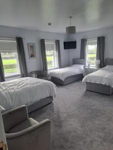 a bedroom with three beds and a chair and windows at New Lisnagalt Lodge in Coleraine