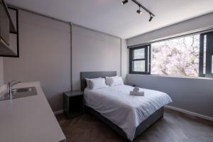 um quarto com uma cama branca e uma janela em Inn & Out Plus Rosebank em Joanesburgo